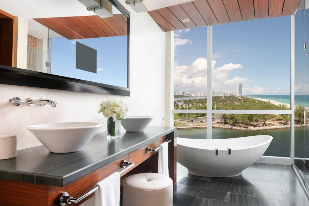 Modern hotel bathroom with a freestanding bathtub, double sinks, and floor-to-ceiling windows with ocean views